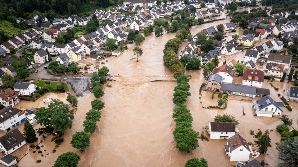 A tree-lined village street flooded with water.